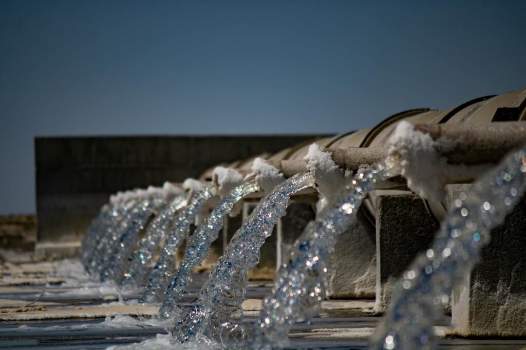 INNAQUA ingeniería civil Madrid Close-up view of water flowing from industrial pipes against a clear blue sky.